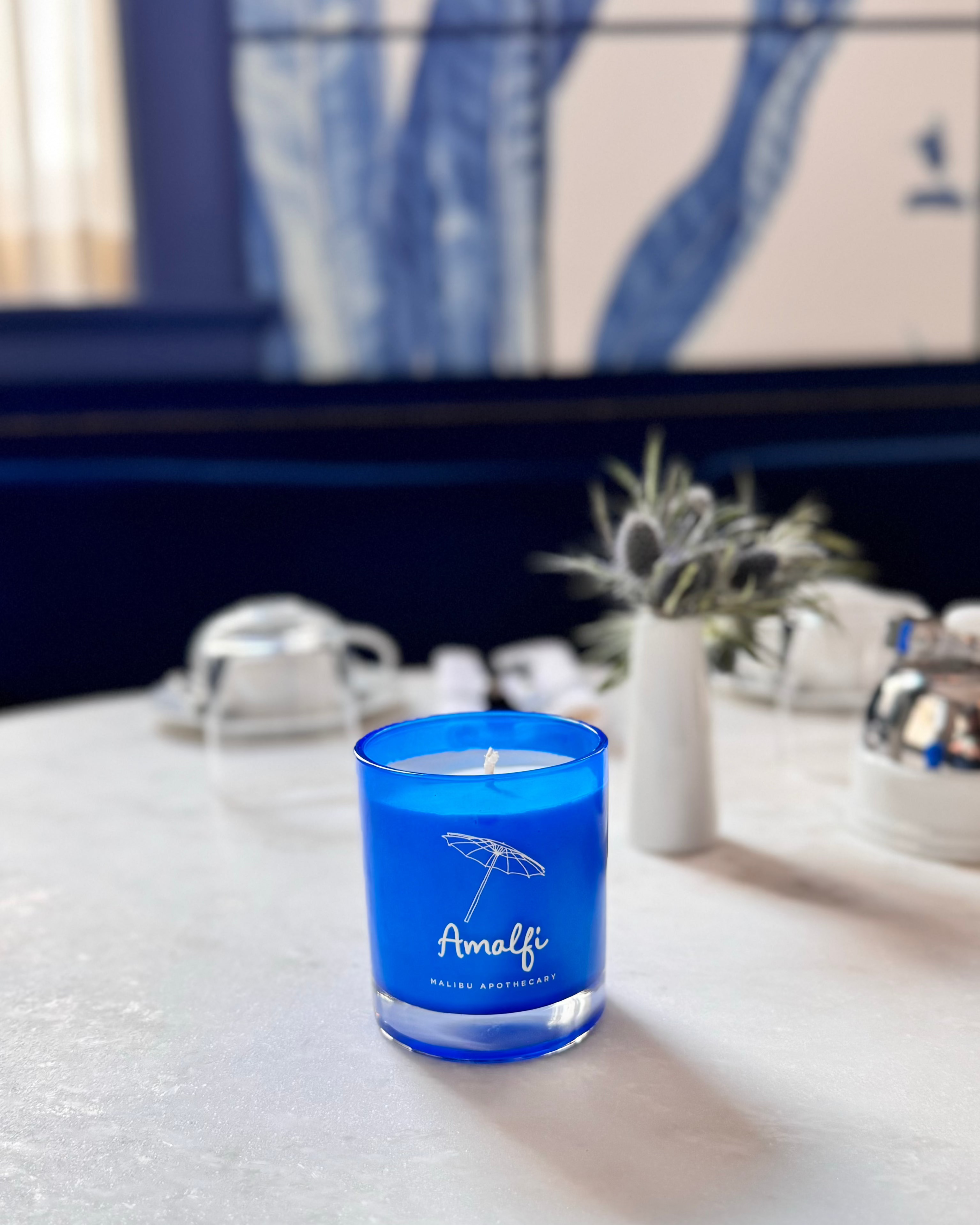 A scented candle with notes of basil and arugula inspired by the Amalfi coast in a bright blue acqua glass jar