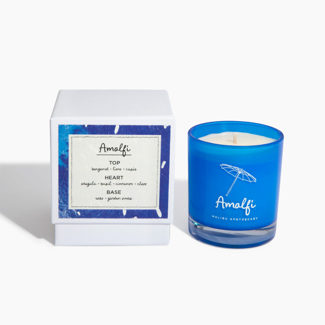 Amalfi candle in bright blue glass jar with umbrella logo alongside matching ingredients card packaging listing top, heart and base notes, made with all natural coconut and soy wax