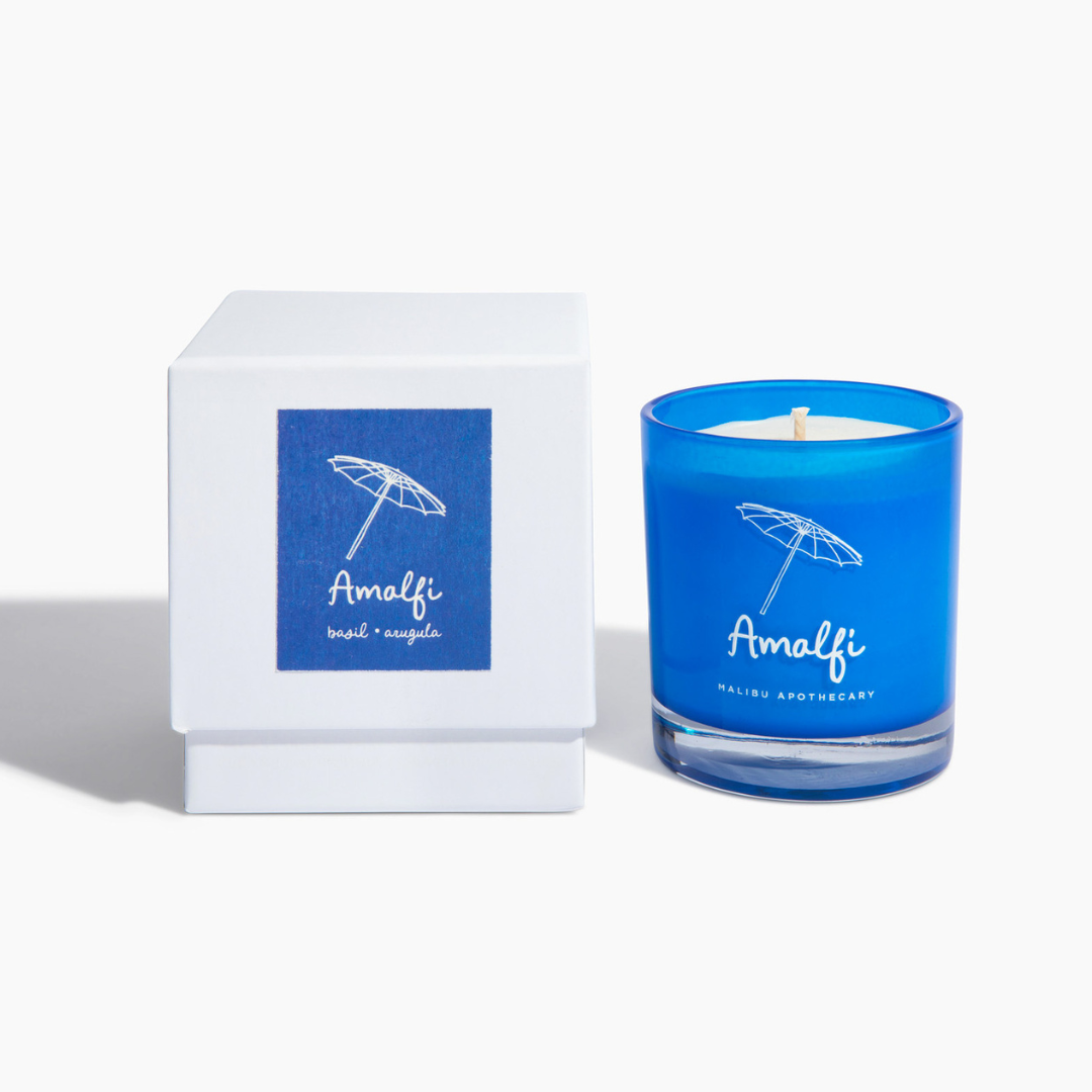 Amalfi candle in bright blue glass jar with umbrella logo paired with white box featuring matching umbrella graphic, made with all natural coconut and soy wax