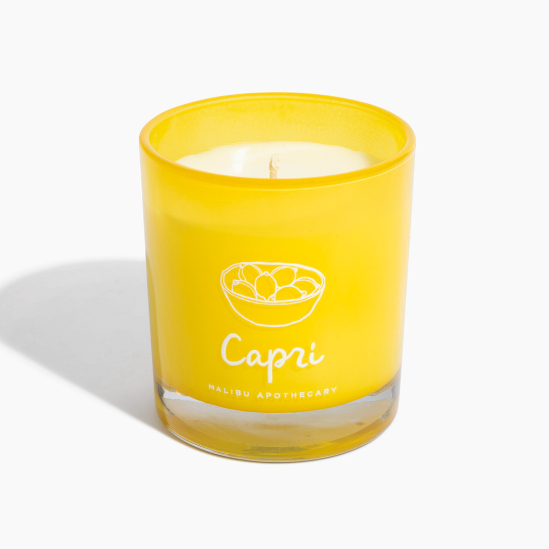 Capri candle in bright yellow glass jar with Capri lemon bowl logo, made with all natural coconut and soy wax and scented with lemon peel, lime, and sage, photographed against white background