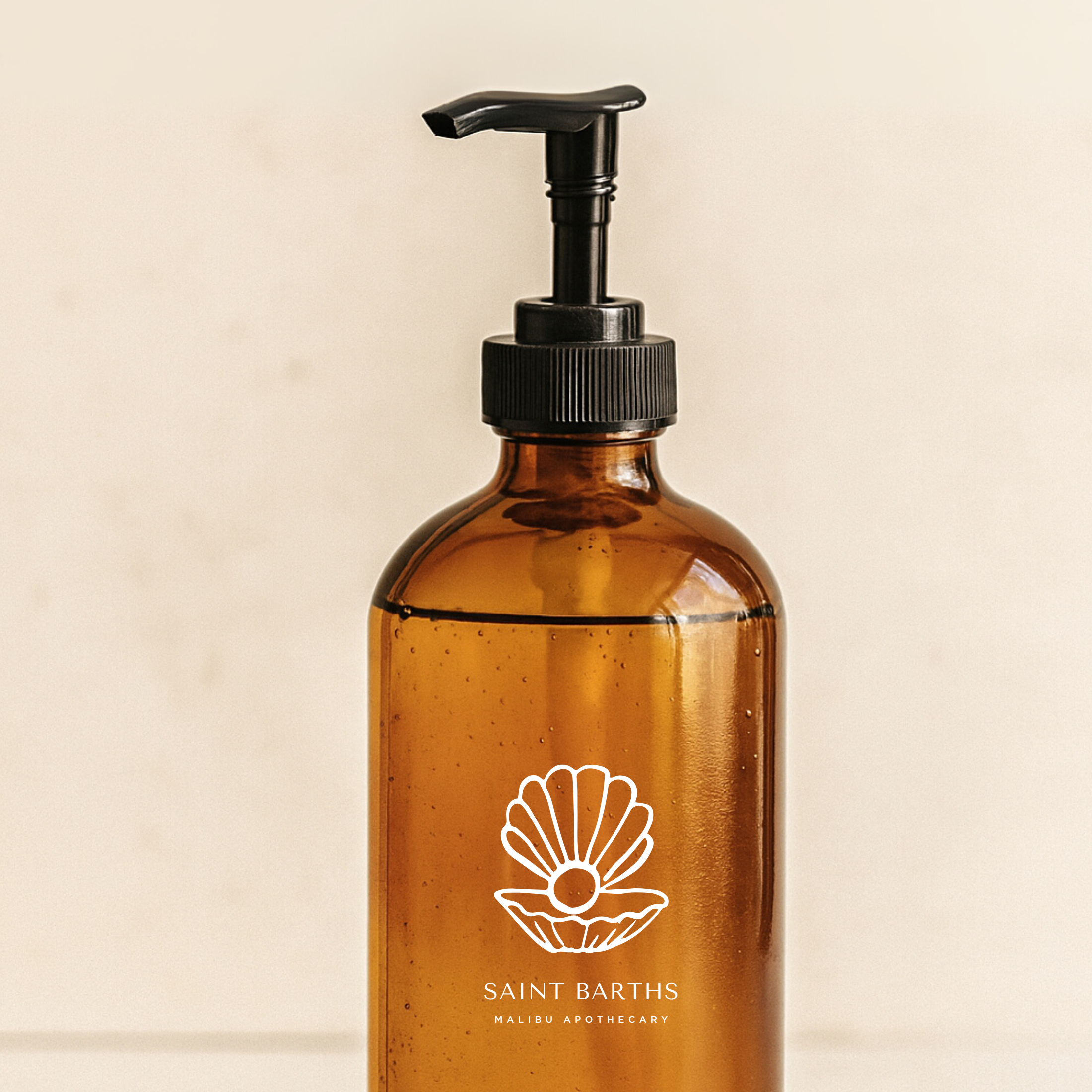 Amber glass pump bottle of Malibu Apothecary Saint Barths hand wash with black pump and shell logo against beige background; luxury clean nontoxic custom hand wash