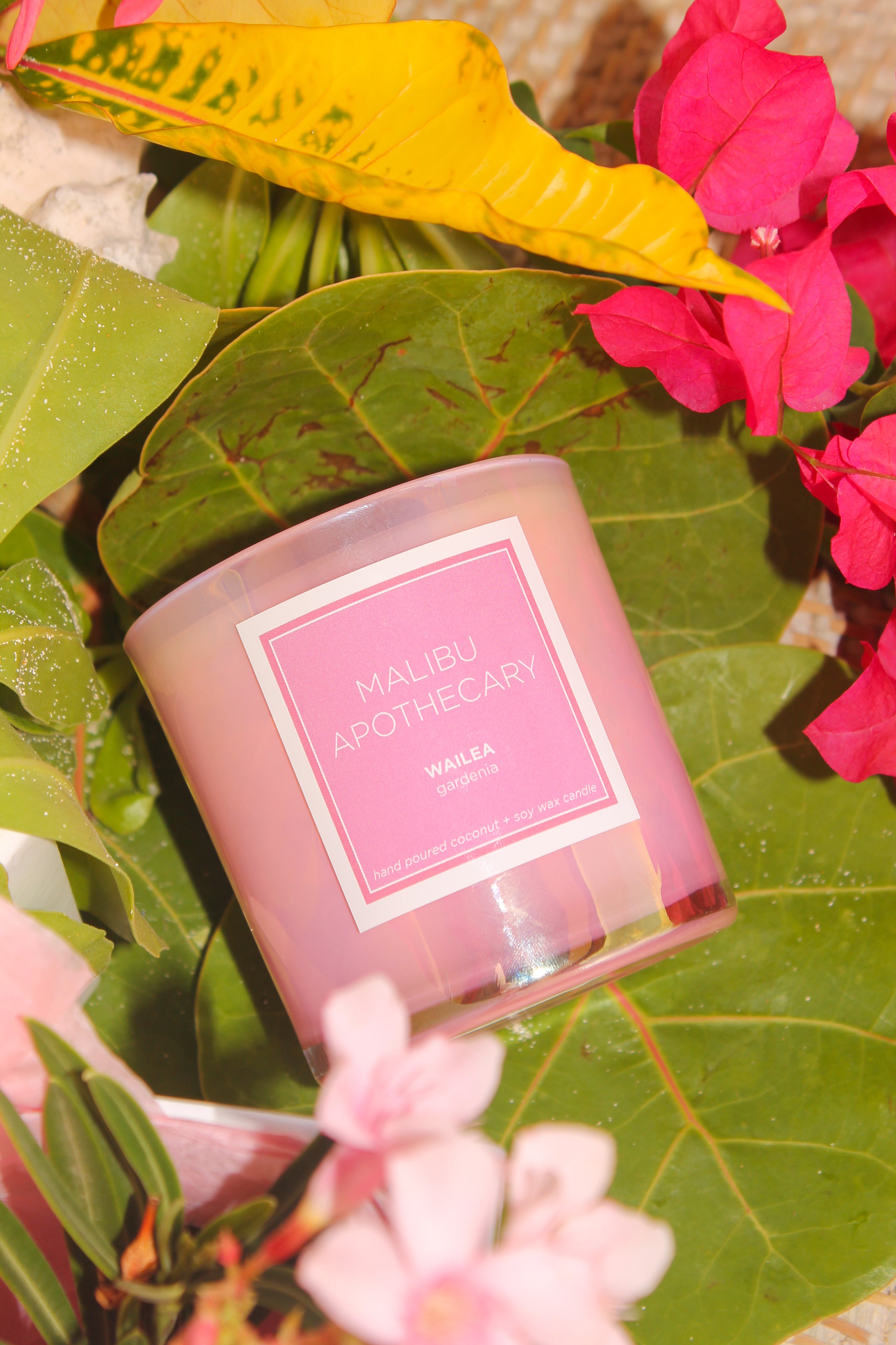 Pink candle with a label in a natural setting with green leaves and pink flowers