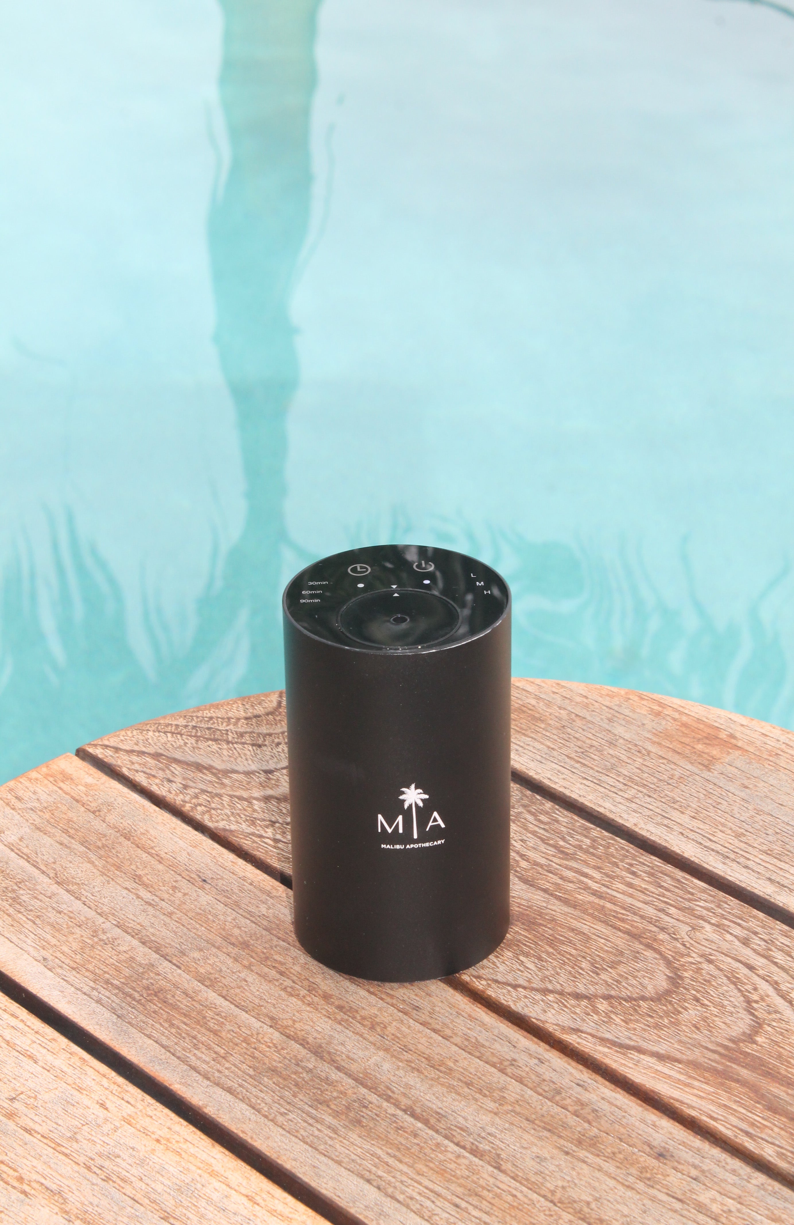 ScentSolution Mini portable black scent diffuser on a wooden pool deck beside turquoise swimming pool water, reflecting a spa-like outdoor lifestyle; ideal for diffusing pure aroma oils.
