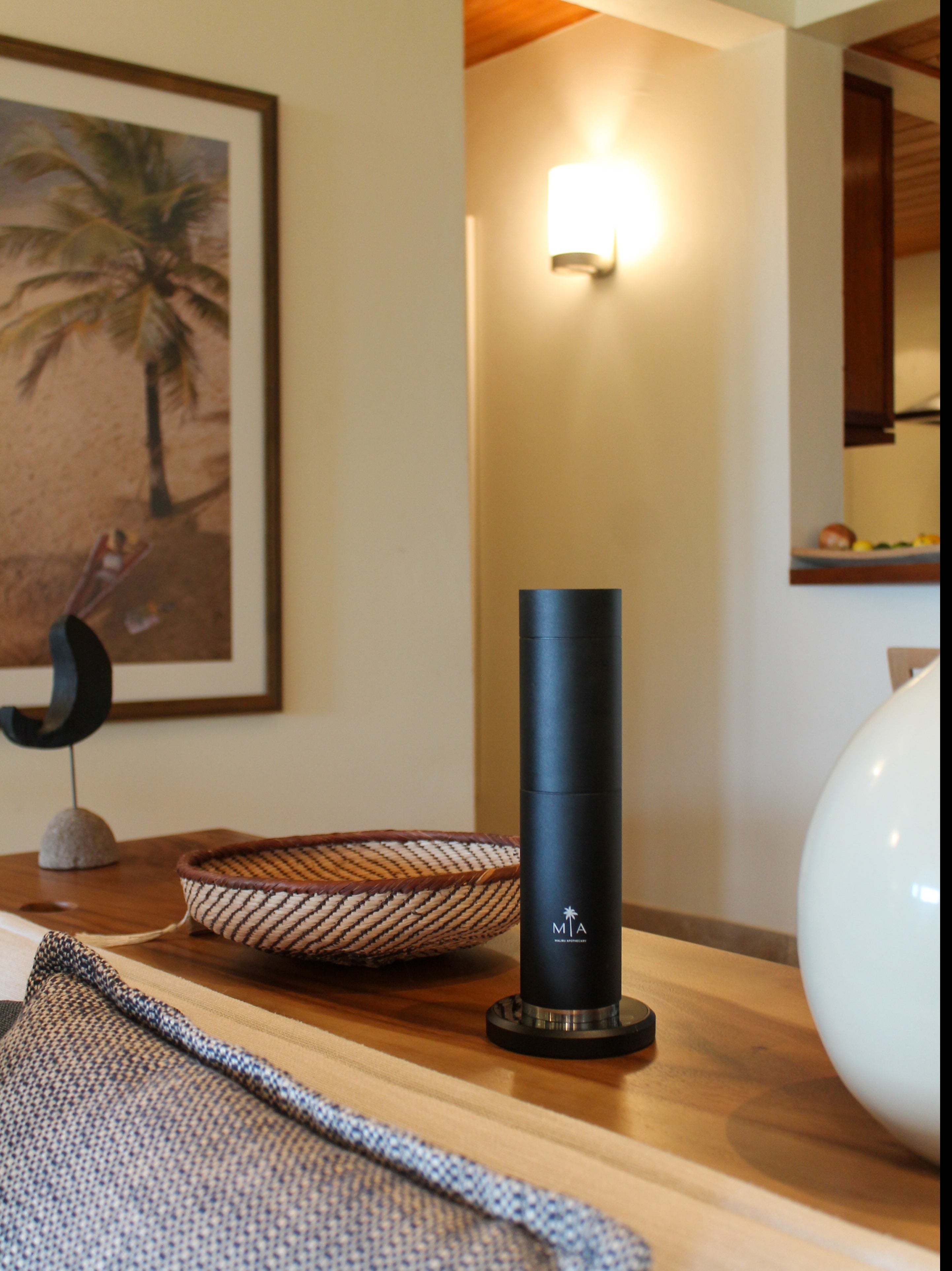 ScentSolution Pro diffuser on a wooden table in a warm modern home interior with wicker bowl and neutral decor, offering heatless nebulizing fragrance diffusion for luxury homes