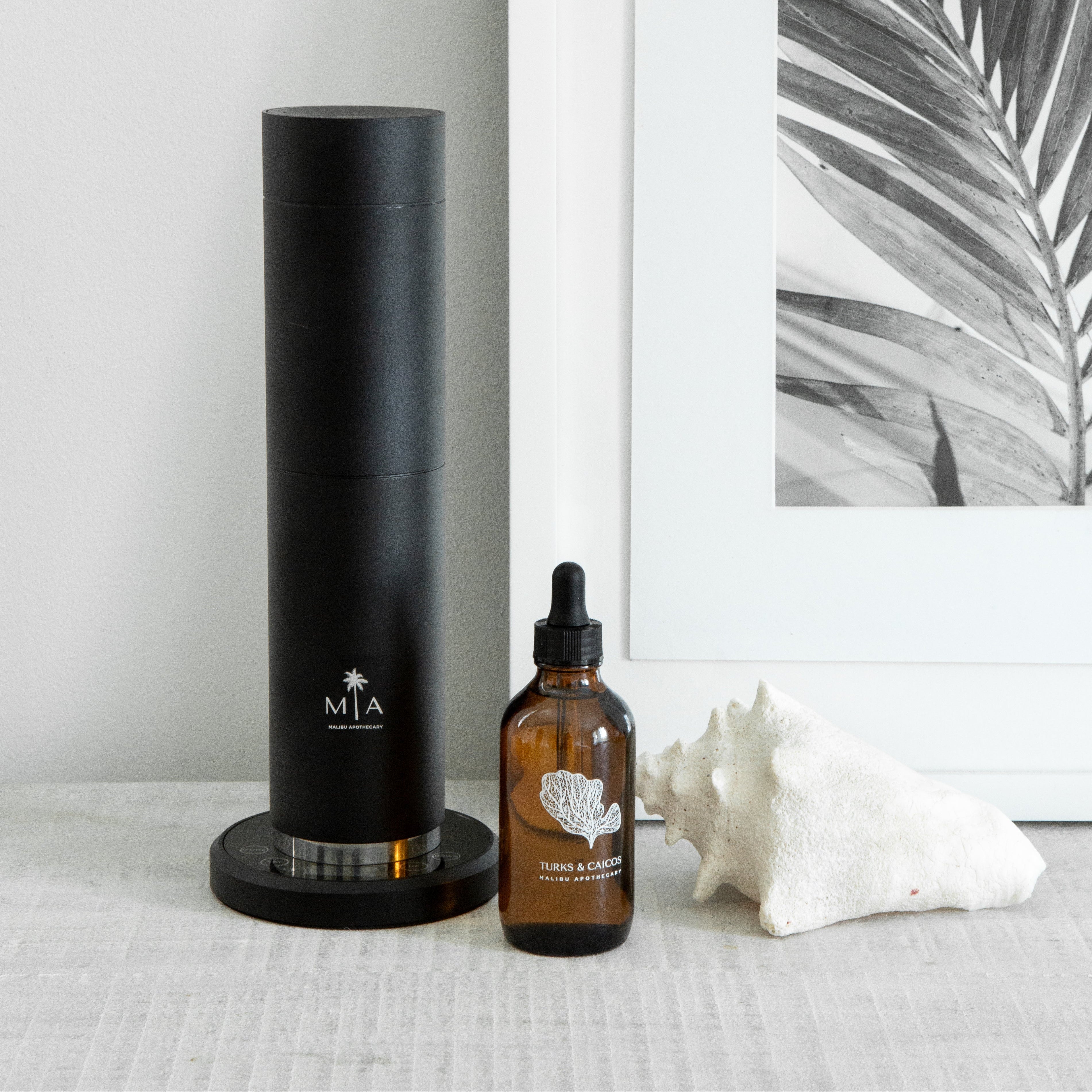 ScentSolution Pro diffuser with pure aroma oil dropper and seashell on minimalist tabletop, using nebulizing technology for luxury home fragrance
