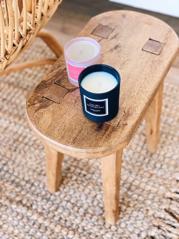 Malibu Apothecary's Iridescent Pink candle with a holographic effect next to a matte black candle sitting on a wooden table with a rattan rug and chair