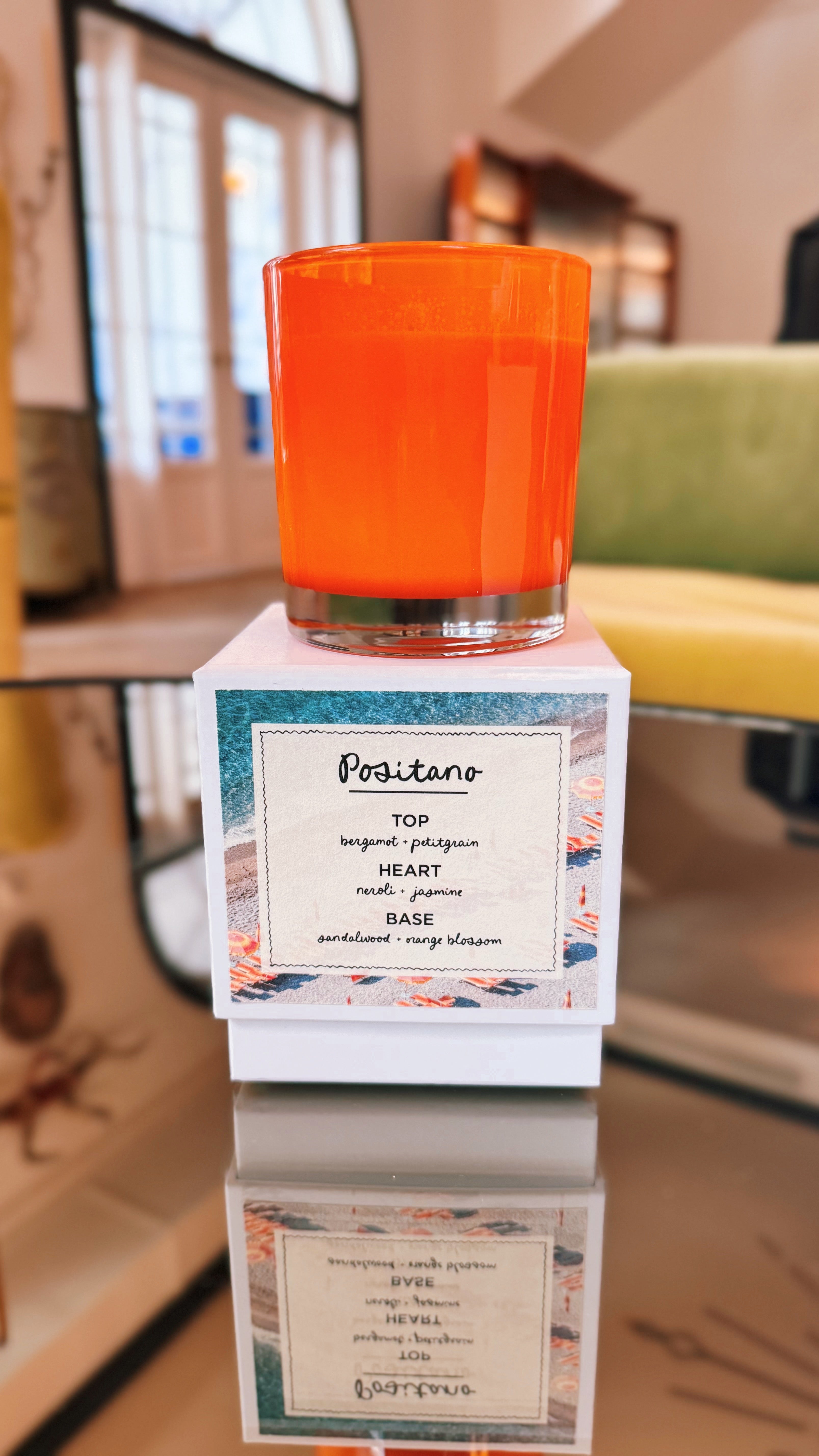 Positano candle on gift box in elegant living room, reflecting on glass table with neroli and orange blossom scent in coconut soy wax