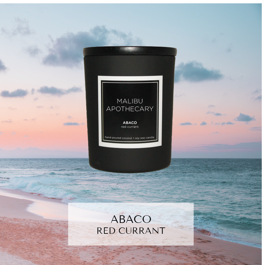 Mini black Malibu Apothecary candle labeled Abaco red currant set against pink sand beach and turquoise ocean with pastel sunset sky, made with all natural coconut and soy wax