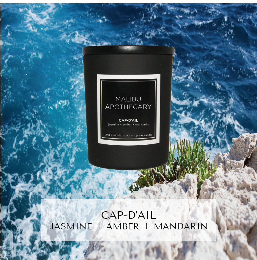 Mini black Malibu Apothecary candle labeled Cap d’Ail jasmine + amber + mandarin set on rocky Mediterranean coastline with swirling blue sea, made with all natural coconut and soy wax