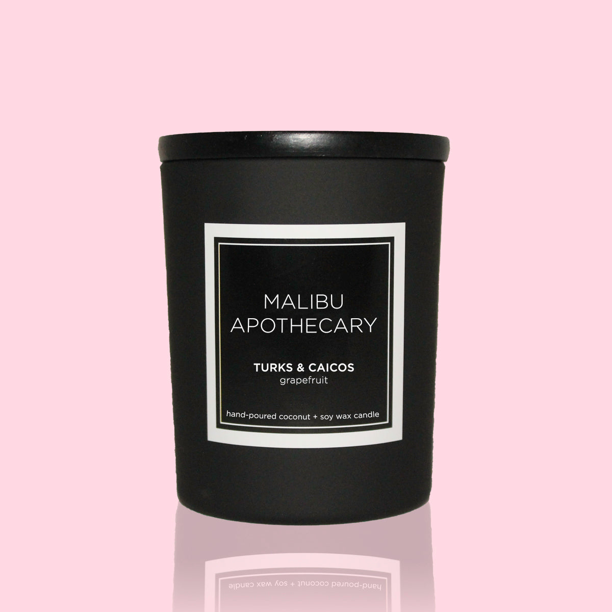 Mini black Malibu Apothecary candle labeled Turks & Caicos grapefruit with coconut and soy wax on reflective surface, set against pastel pink background