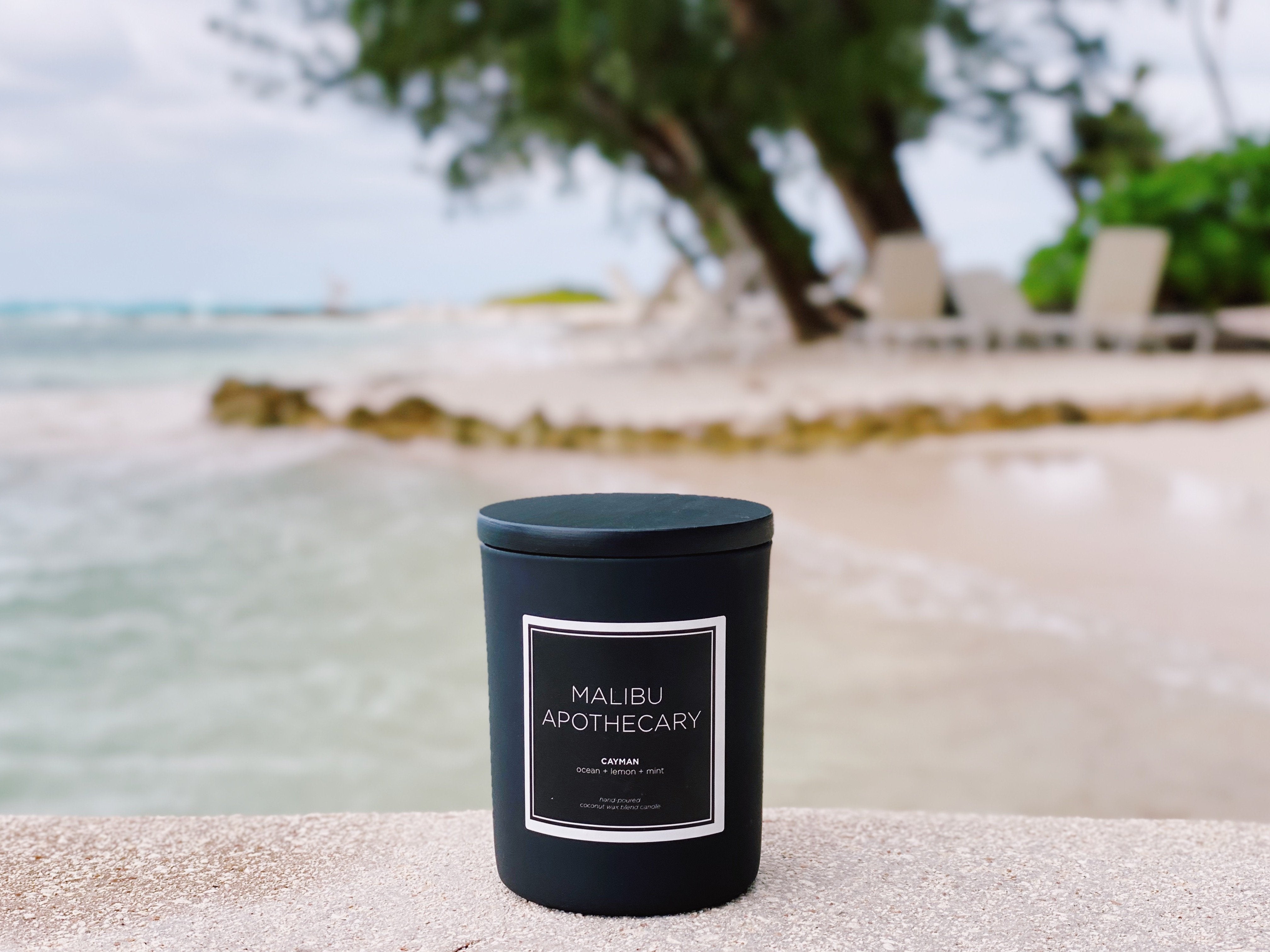 Malibu Apothecary's Cayman scented candle with notes of lemon and mint sitting on a rock at Rum Point in the Cayman Islands 
