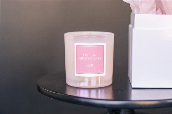 Iridescent Pink Candle in the Abaco Bahamas scent of red currant on a black side table with a white gift box and pink tissue paper