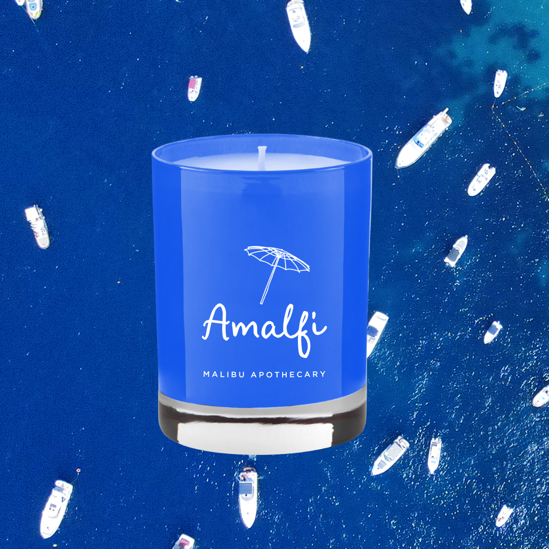 Amalfi blue glass candle floating above an aerial view of boats in deep blue Mediterranean sea, representing basil and arugula notes; made with all natural coconut and soy wax