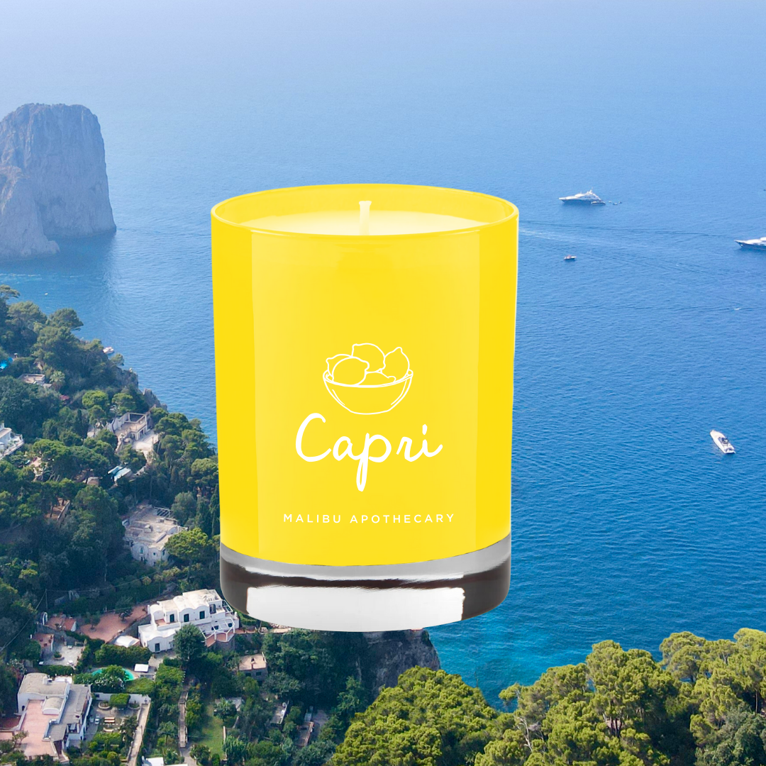 Capri candle in vibrant yellow glass jar superimposed over an aerial view of Capri coastline with blue Mediterranean sea, cliffs and boats, representing lemon peel and sage fragrance; made with all natural coconut and soy wax