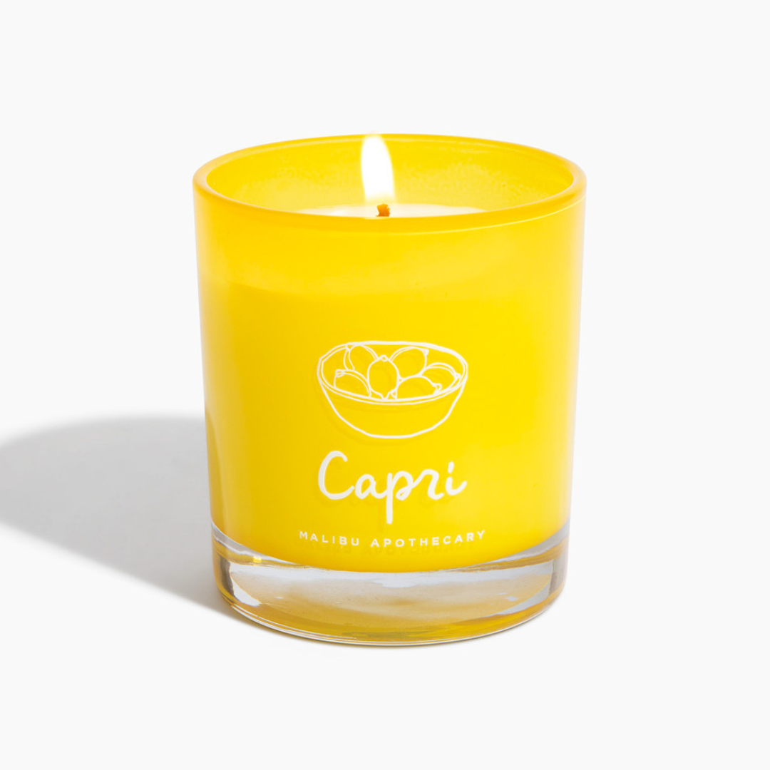 Capri candle burning in vibrant yellow glass jar featuring hand-drawn lemon graphic and white Capri logo, crafted with all natural coconut and soy wax and scented with lemon peel and sage