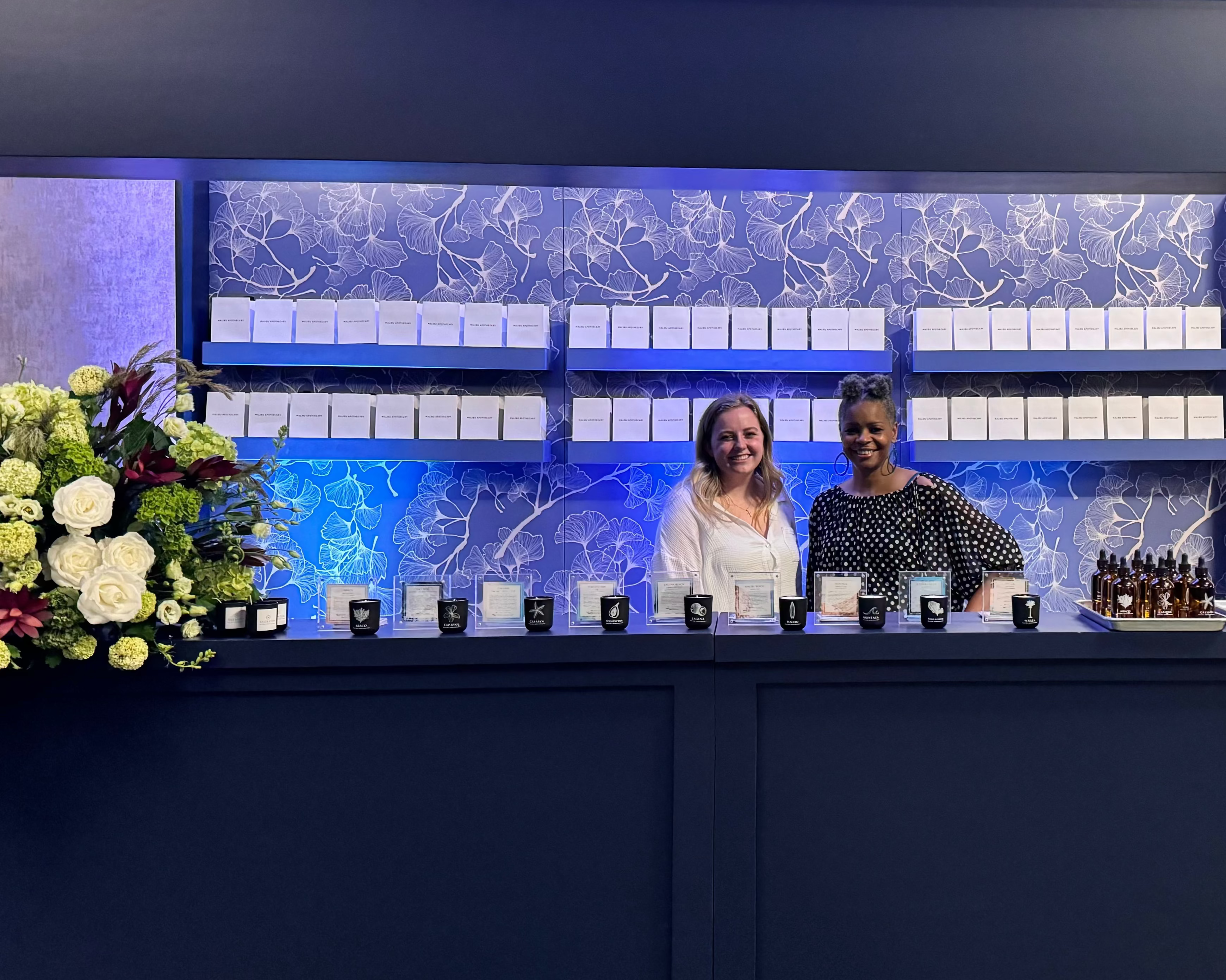 Two people standing behind a mobile candle mixology bar with a blue display and floral arrangement at a Sheraton for a corporate event activity idea