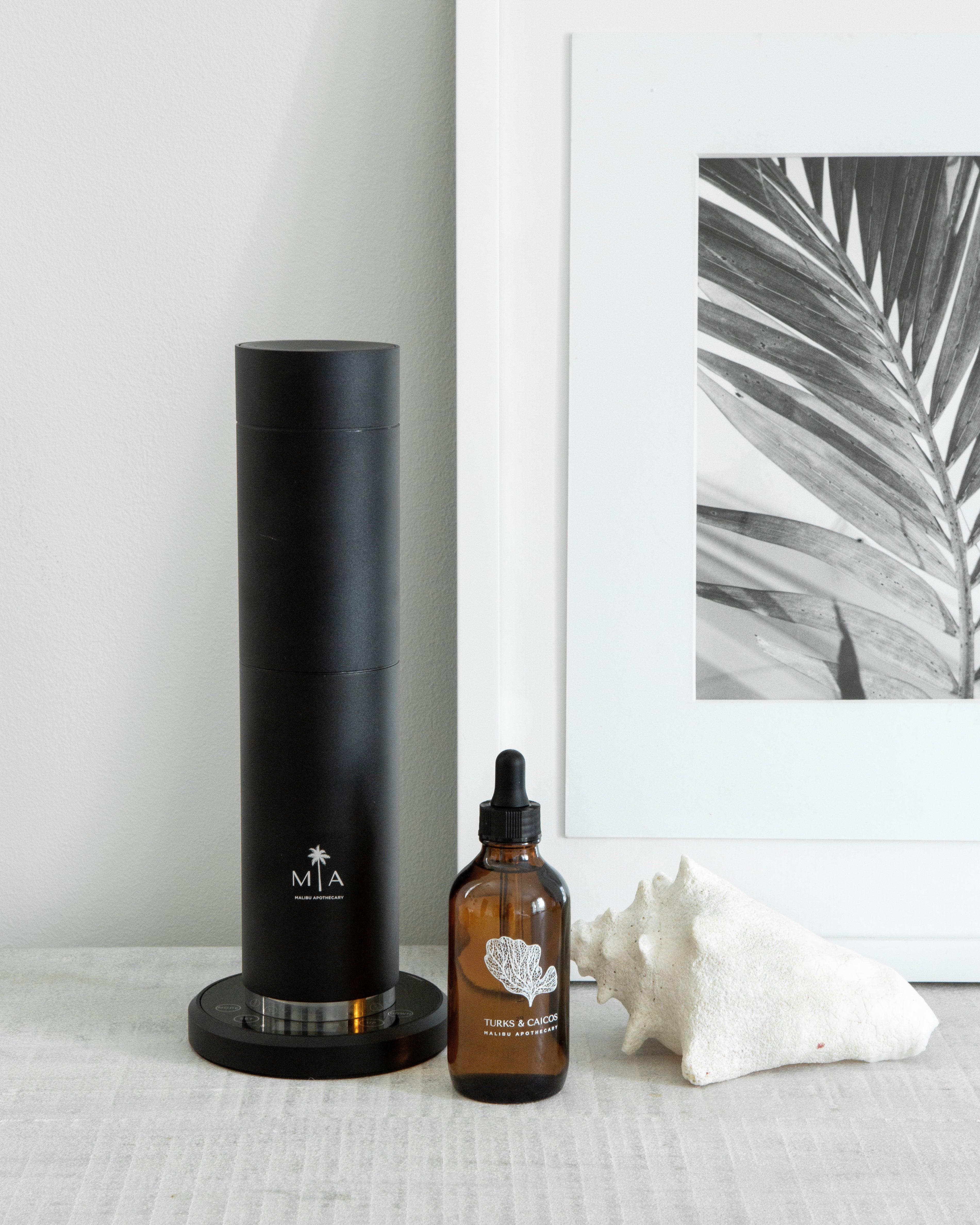 ScentSolution Pro diffuser with pure aroma oil dropper and seashell on minimalist tabletop, using nebulizing technology for luxury home fragrance