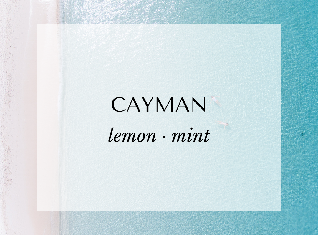 Text 'CAYMAN lemon mint' on a light blue background of an aerial ocean shot taken over seven mile beach showcasing Malibu Apothecary's clean herbal scents