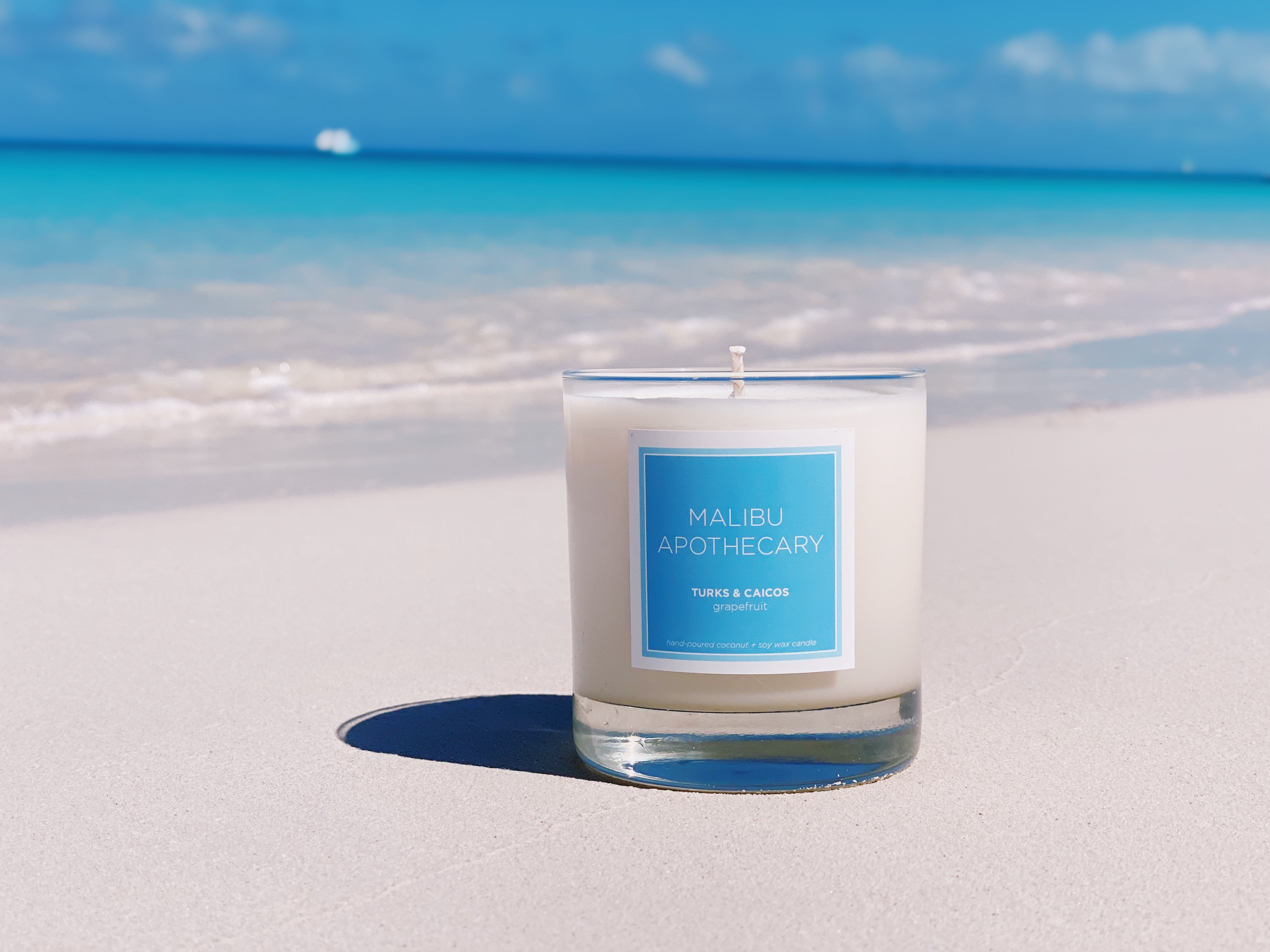 Candle with a blue label on a sandy beach with ocean in the background
