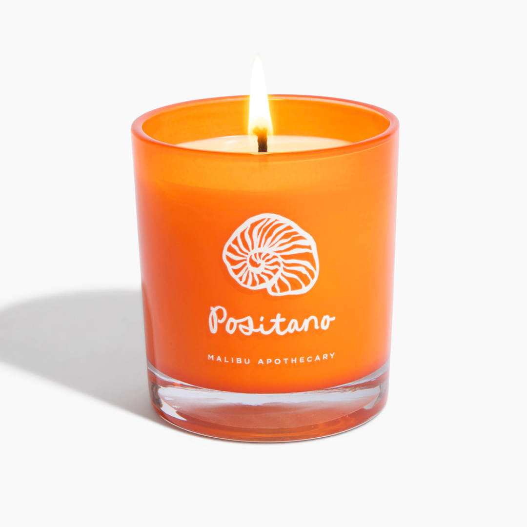 Positano neroli and orange blossom candle in vibrant orange glass jar with shell logo, lit against white background, hand-poured with all natural coconut and soy wax