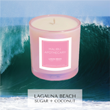 Laguna Beach candle with notes of sugar, coconut, and vanilla, in iridescent pink in front of wave